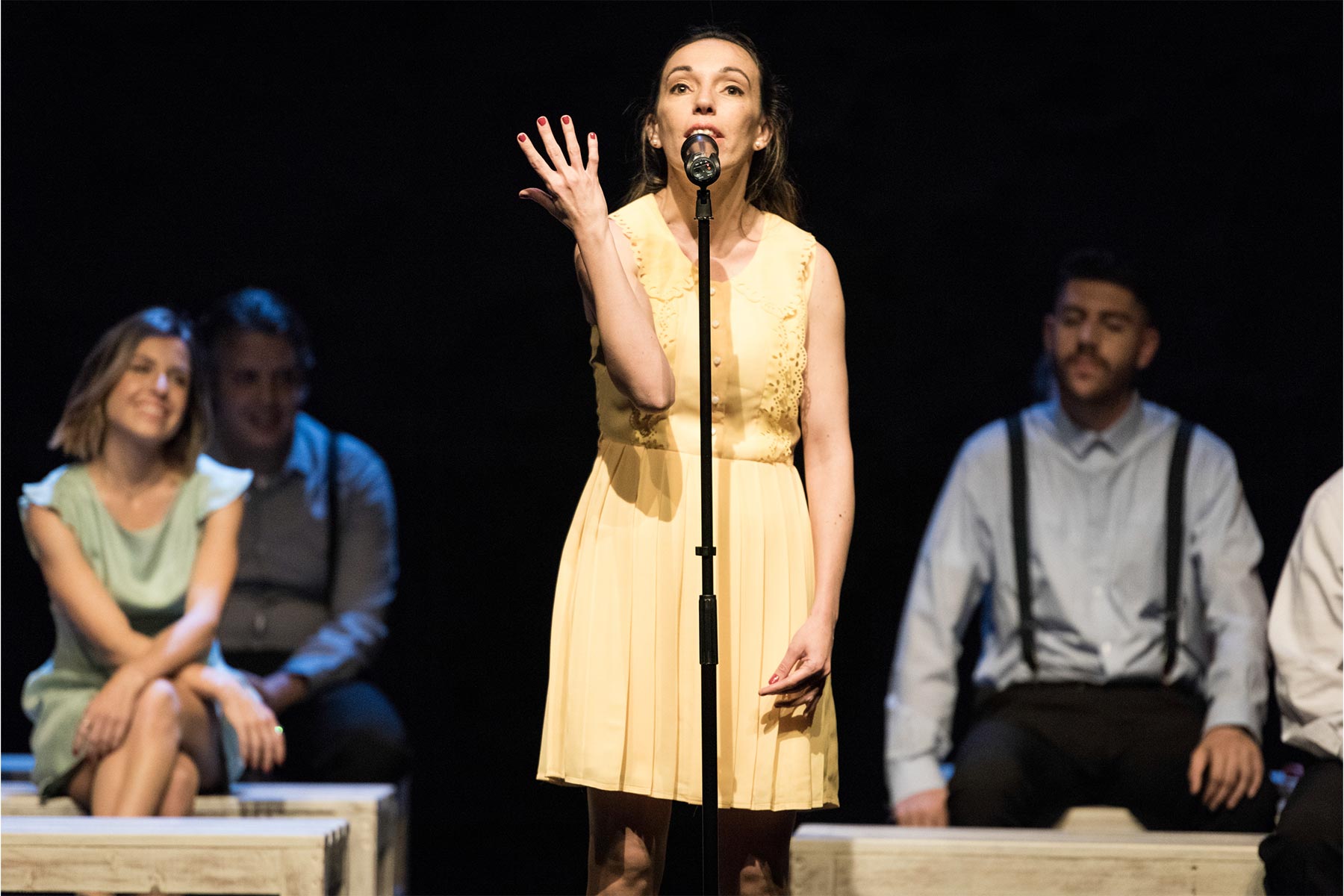 Soprano en escena con grupo teatral, actriz en teatro, interpretación artística en vivo, Andrea Jiménez en actuación teatral, arte dramático y performance en escenario.