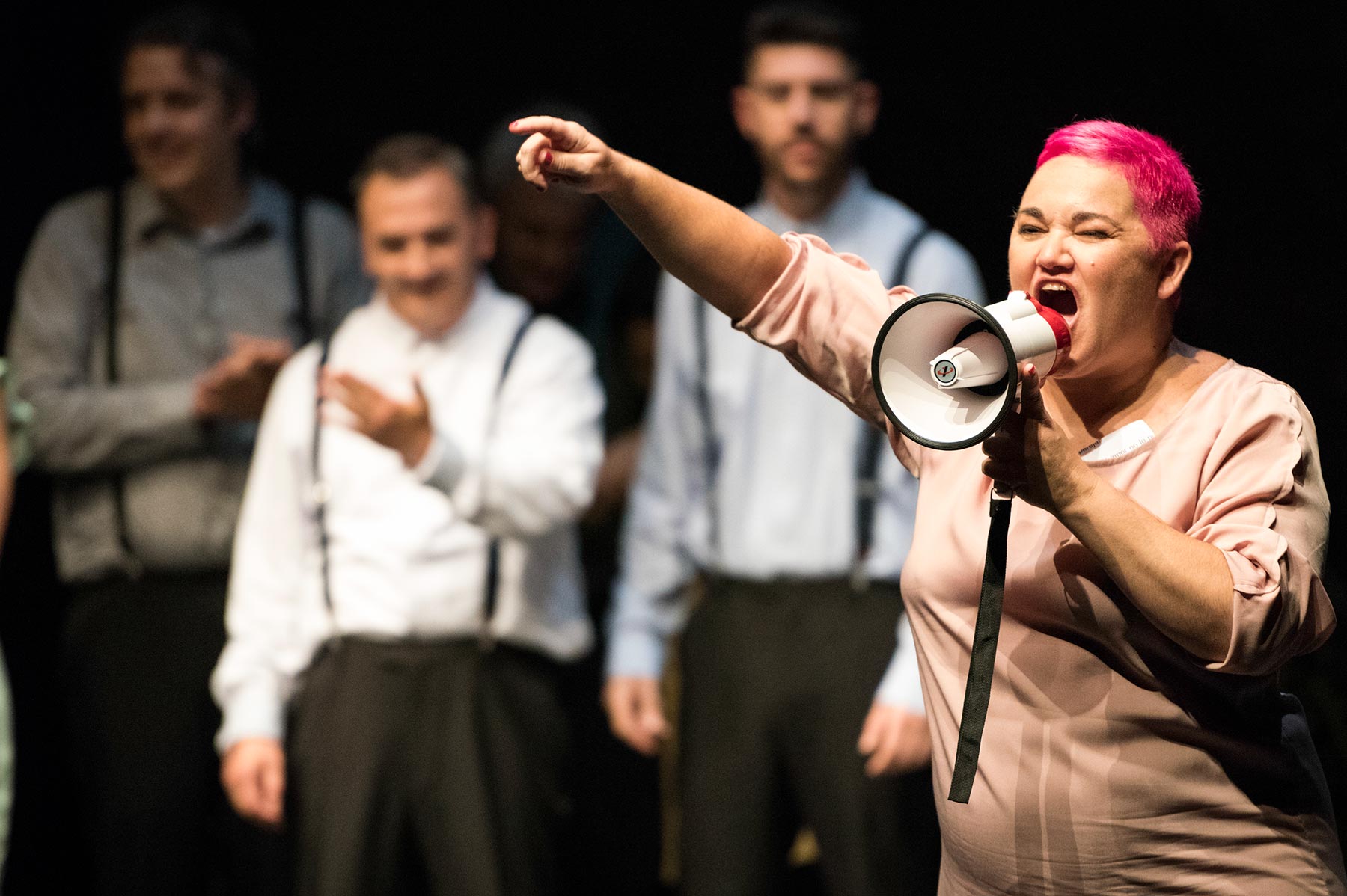Dama con pelo rosa usando megáfono en escenario, expresando emoción y liderazgo en evento de motivación o protesta.