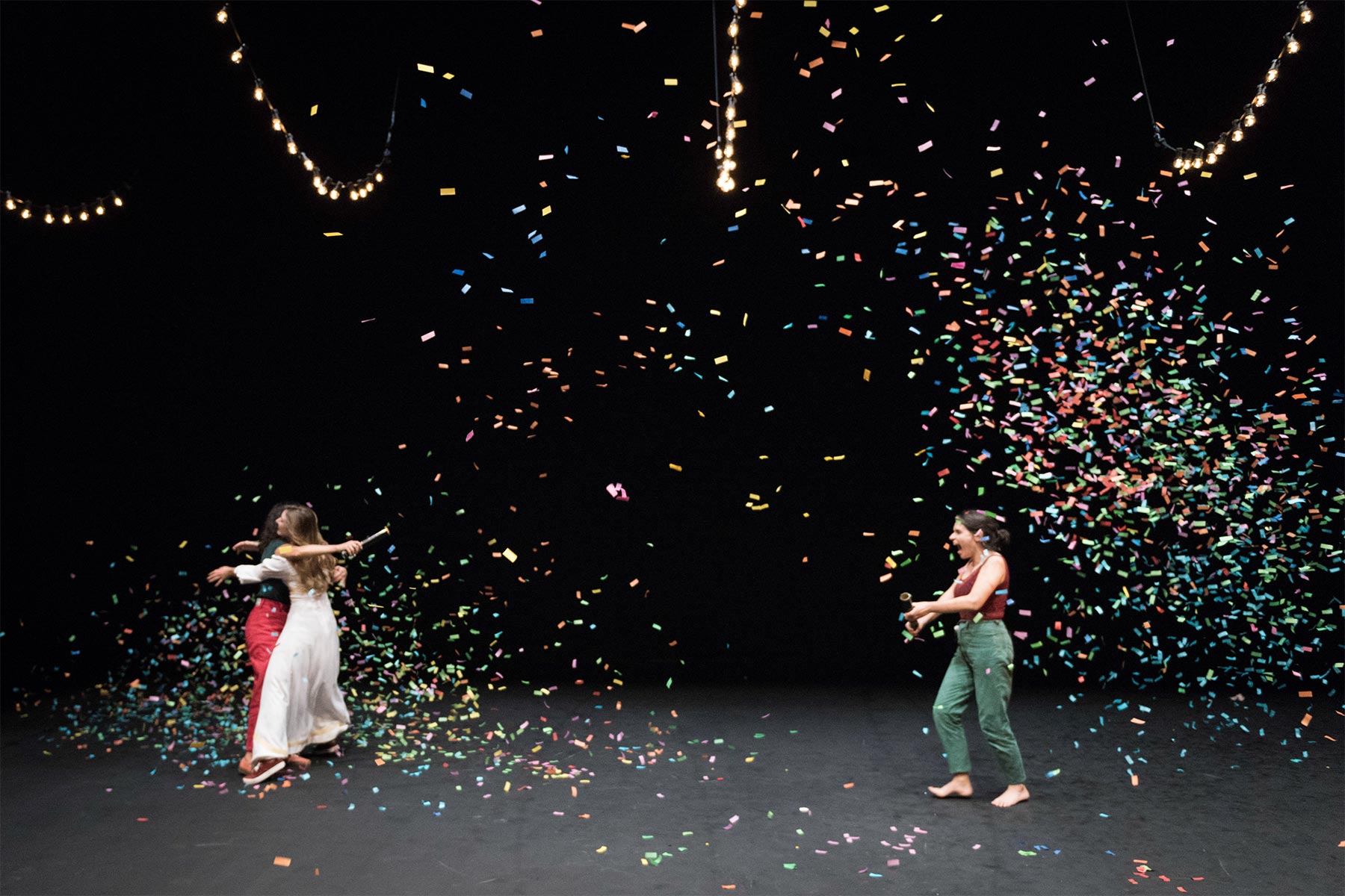 Explosión de confeti durante un evento de celebración en un escenario oscuro con luces y personas disfrutando del momento.