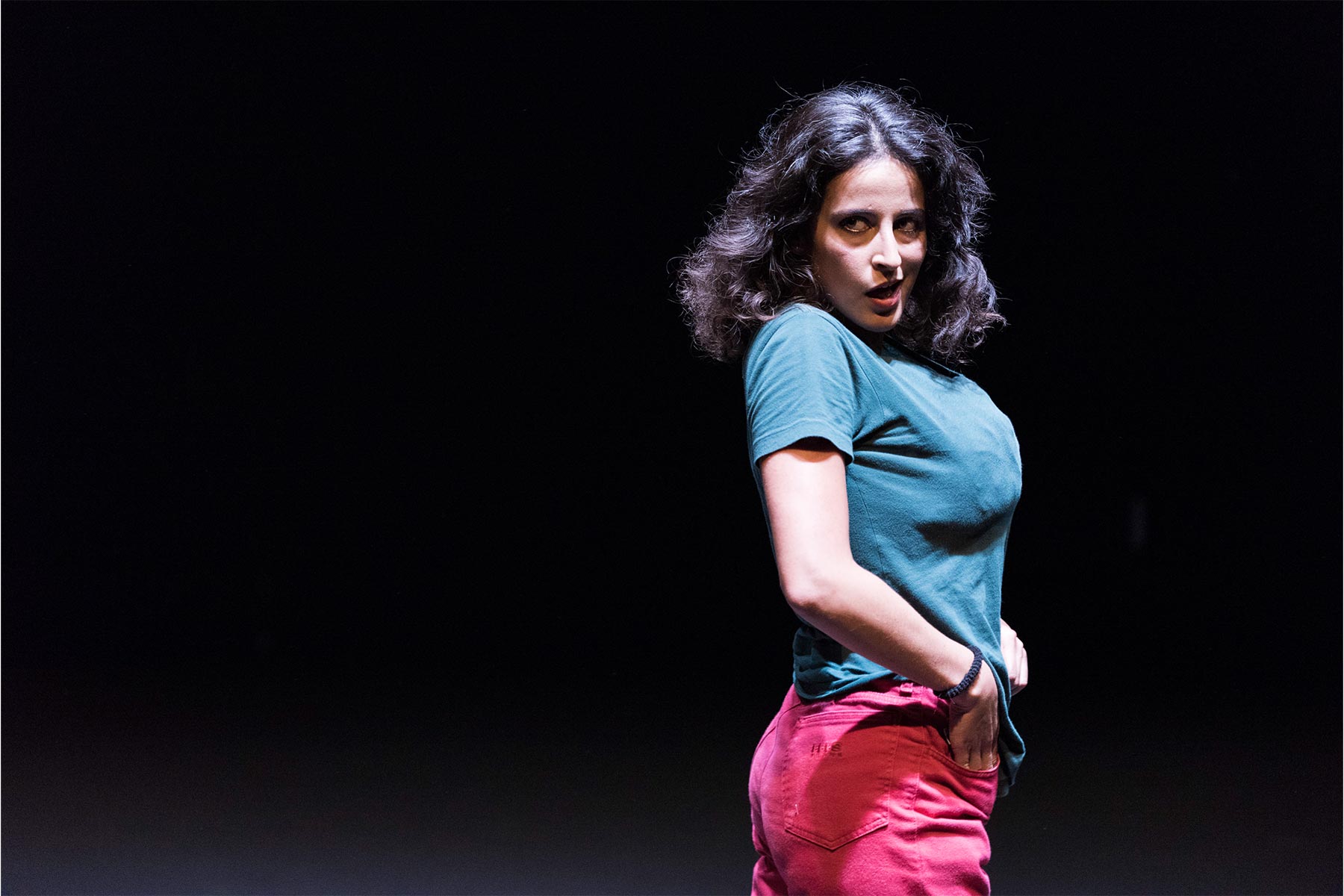 Voz en off de mujer en escena de teatro, moda y estilo, Andrea Jiménez, actriz y artista en vivo, expresando emoción y energía en su espectáculo teatral, con ropa moderna y expresión convincente.