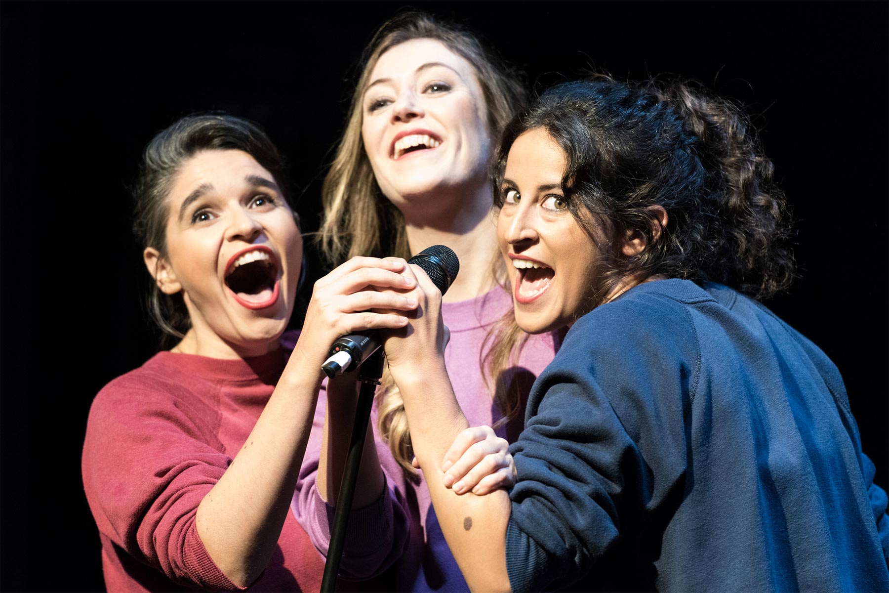 Chicas cantando y actuando en un escenario, tomando el micrófono juntas, transmitiendo energía y entusiasmo, en un ambiente de espectáculo y diversión, ideal para contenido de entretenimiento y talento femenino.