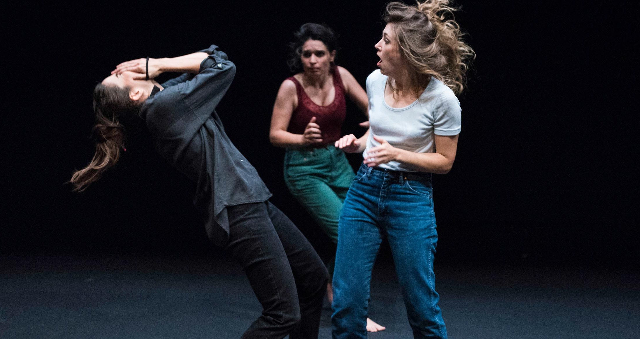 Actrices en una obra de teatro, expresando emociones intensas en escena, con iluminación dramática y fondo negro, para promover eventos culturales y artes escénicas.