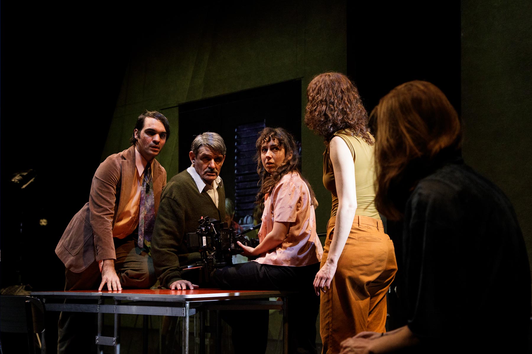 Fotografía de una escena teatral con cinco actores en un escenario oscuro, participando en una grabación o ensayo, mostrando expresión emocional y concentración.