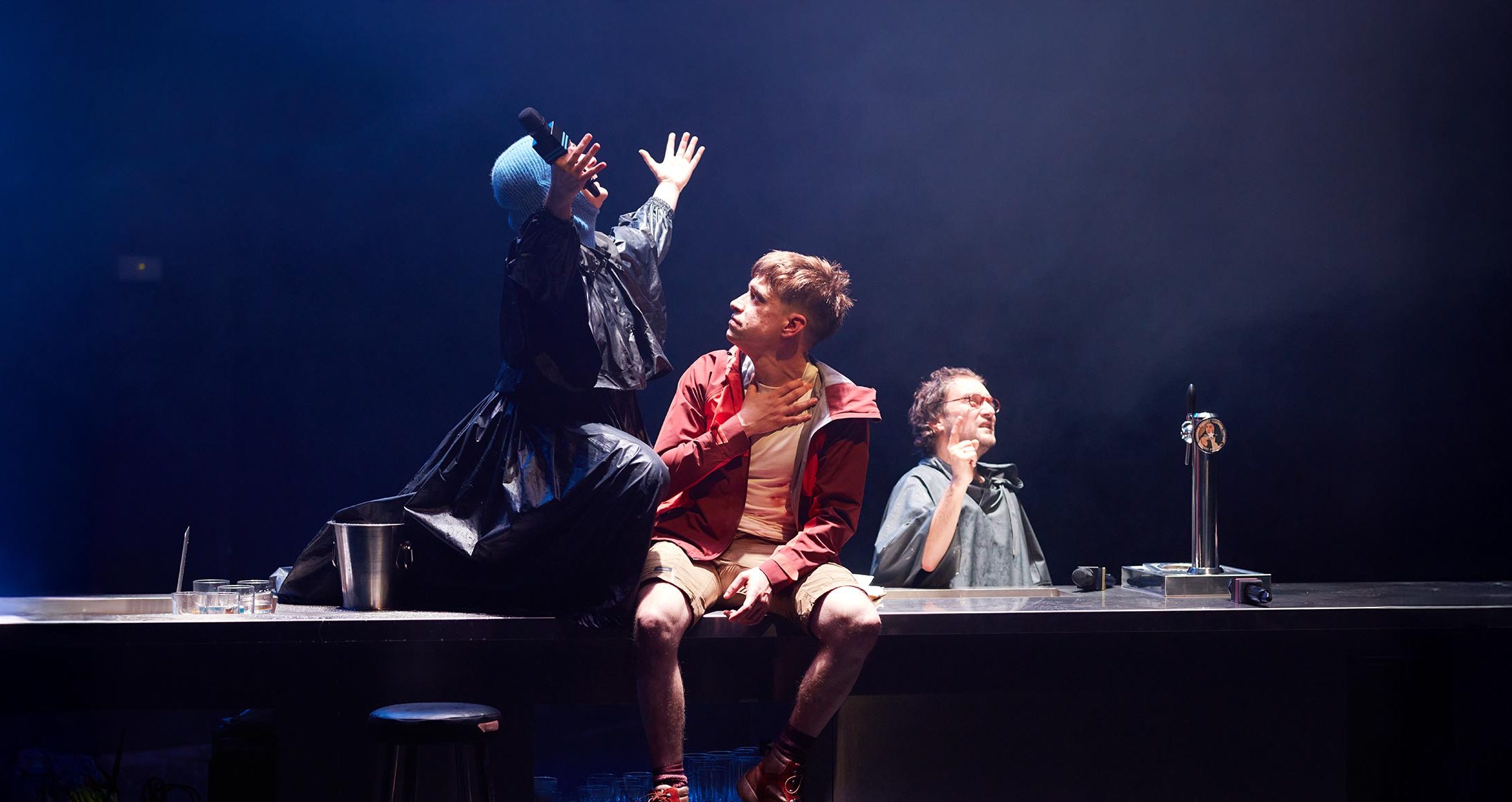 Personajes actuando en una obra teatral en el escenario, con iluminación dramática y ambiente teatral en un teatro contemporáneo.