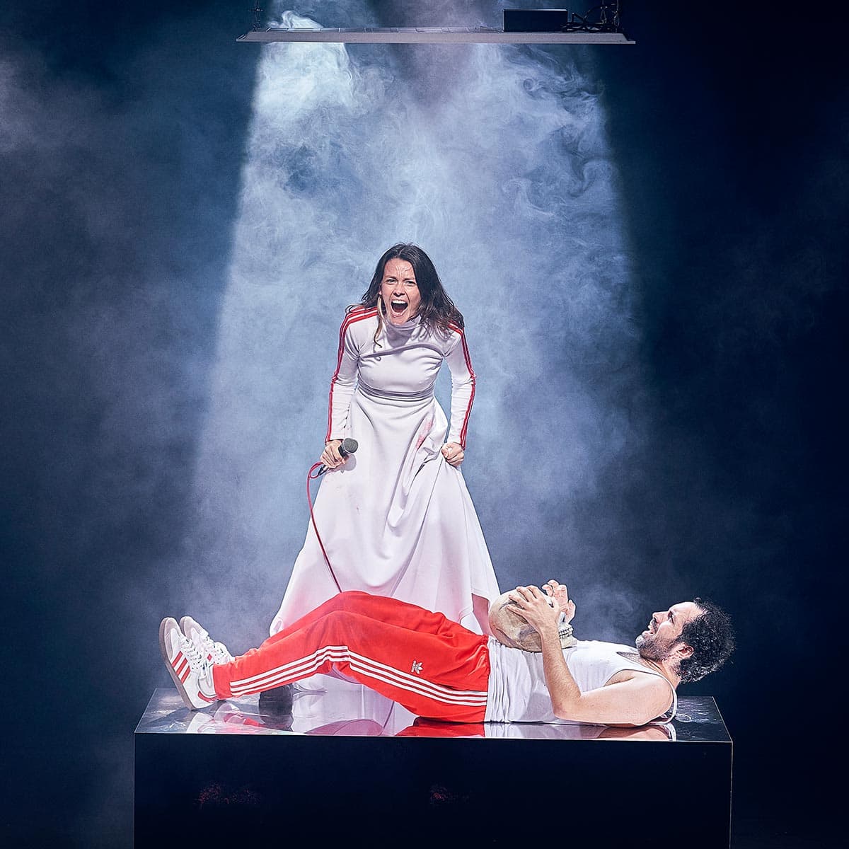 Apoyo emocional y expresión artística en la interpretación teatral de Andrea Jiménez, mostrando pasión y dramatismo en escena con efectos de humo y iluminación profesional.