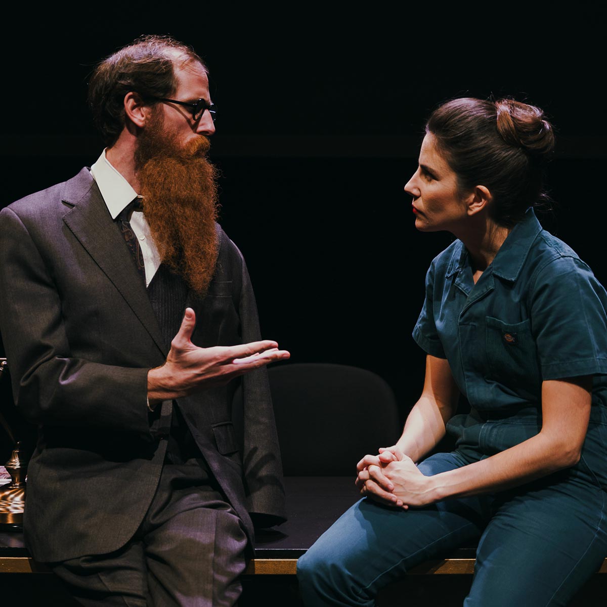Profesores y estudiantes en una clase de teatro, conversando y practicando técnicas actorales, en un ambiente de aprendizaje teatral, con un escenario oscuro de fondo.