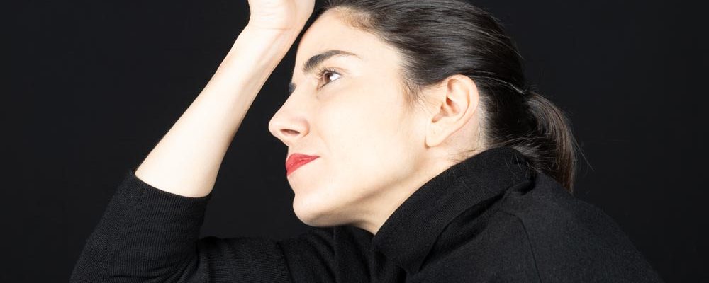 Contemplative woman in black clothing, sitting against black background, thinking mood.