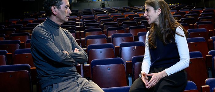 Asiento vacío, interior de teatro o sala de conferencias con dos personas conversando, espacio para eventos, comunicación, diálogo, atención al cliente, ambiente profesional, cultura, aprendizaje, networking.